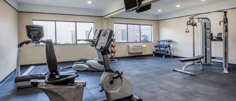 A gym with cardio machines, dumbbells, and a TV mounted on the ceiling.
