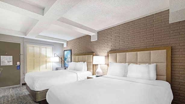 Habitación de hotel con dos camas, una pared de ladrillo, un techo con vigas a la vista y una puerta con un letrero.