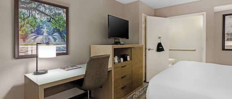A hotel room with a bed, a desk with a computer, a television, a wardrobe, and a framed picture on the wall.