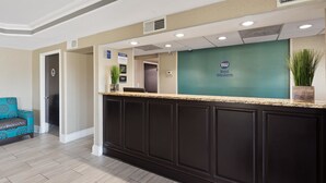 A reception area with a Best Western sign, a reception desk, a waiting area with a blue patterned sofa, and a potted plant. - Best Western Inn (Florence)