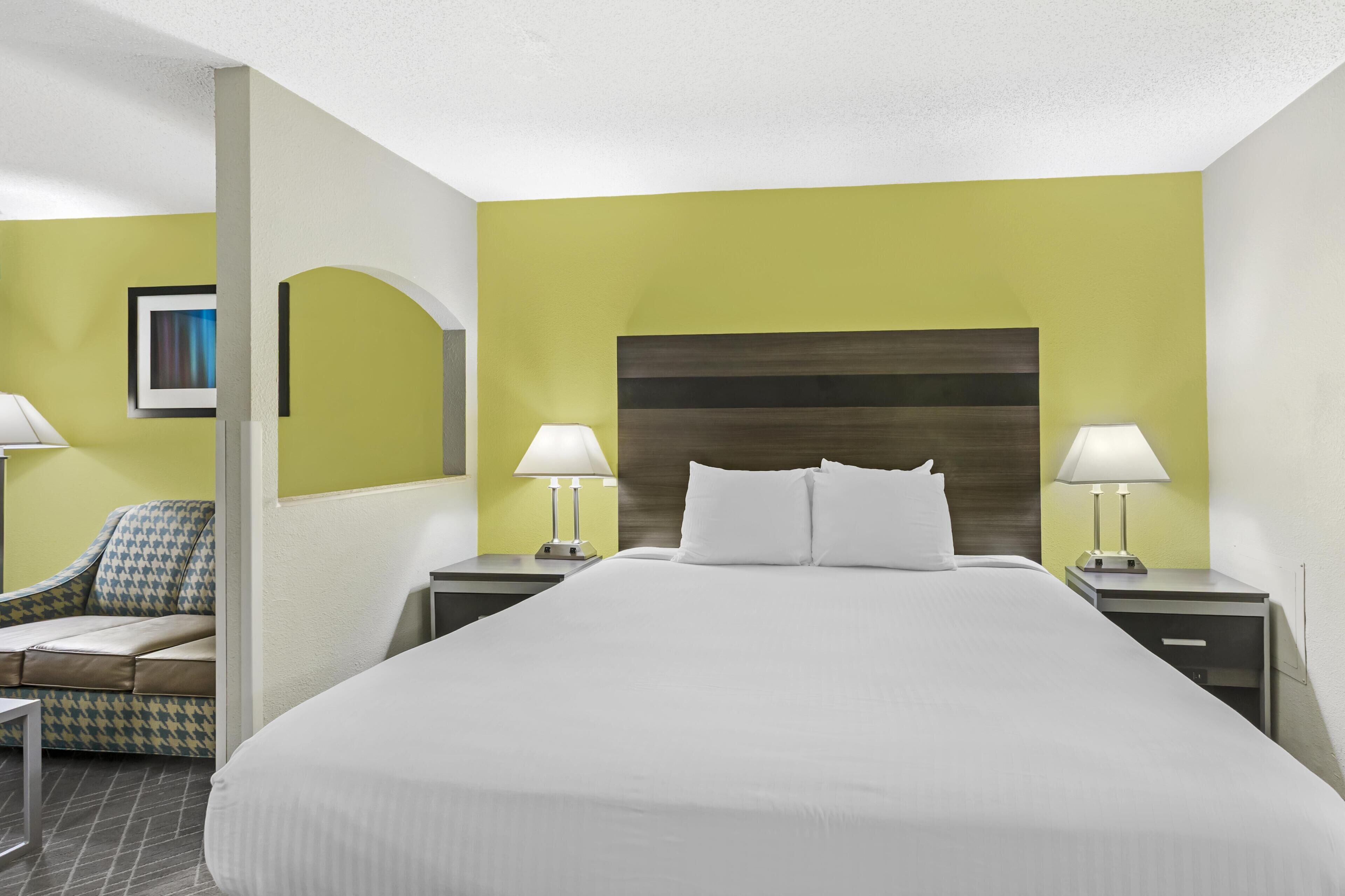Una habitación de hotel con una cama grande, dos mesitas de noche con lámparas, un sofá y un cuadro en la pared.