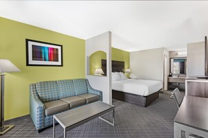 A hotel room with a checkered sofa, a bed, a desk, and a framed picture on the wall.