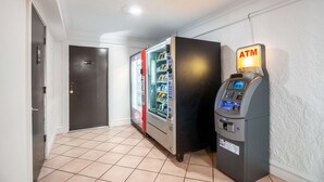 A hallway with an exit sign, a vending machine, and a door. - Motel 6 Hazelwood, MO (Hazelwood)