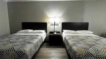 A room with two beds, a nightstand with a lamp, and a wall-mounted light fixture.