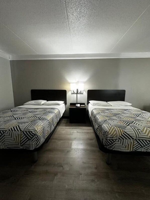 A room with two beds, a nightstand with a lamp, and a wall-mounted light fixture.