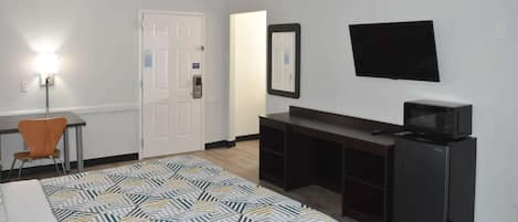 A hotel room with a bed, a desk, a chair, a TV, and a microwave.