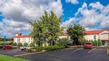 A parking lot with several cars, a building with a red roof, and lush green trees.