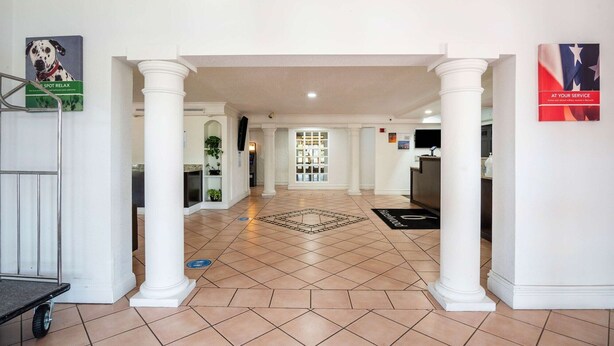 A hotel lobby with a tiled floor, white columns, a reception desk, and a view into the dining area. - Motel 6 Hazelwood, MO (Hazelwood)