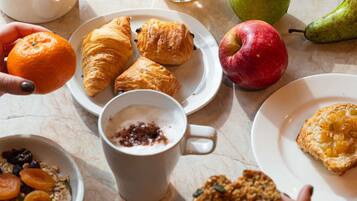 A breakfast setting with croissants, an apple, a pear, a glass of orange juice, a cup of coffee, and a bowl of granola.
