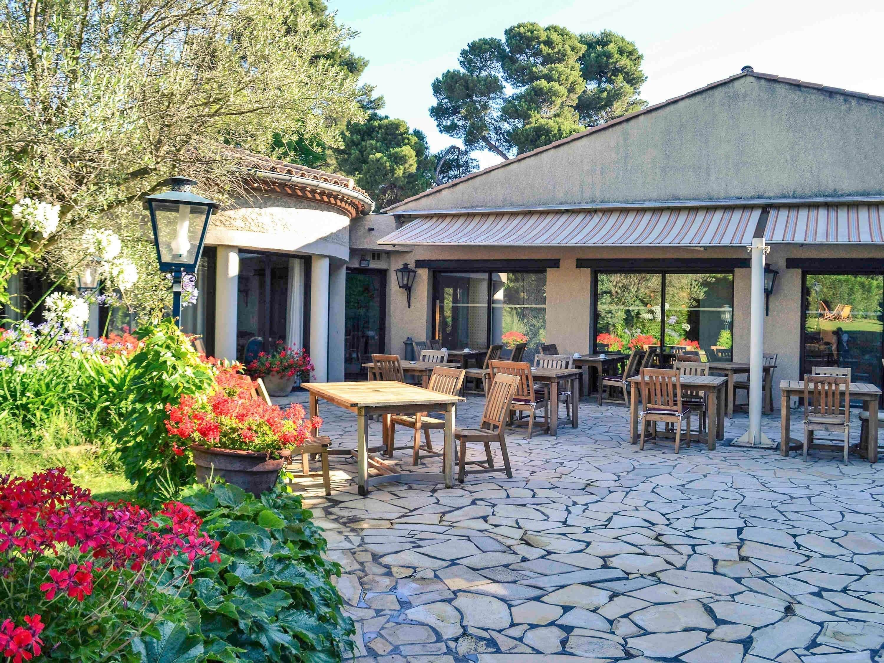 Eine Terrasse im Freien mit Steinboden, Holztischen und -stühlen.