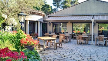 Eine Terrasse im Freien mit Steinboden, Holztischen und -stühlen.