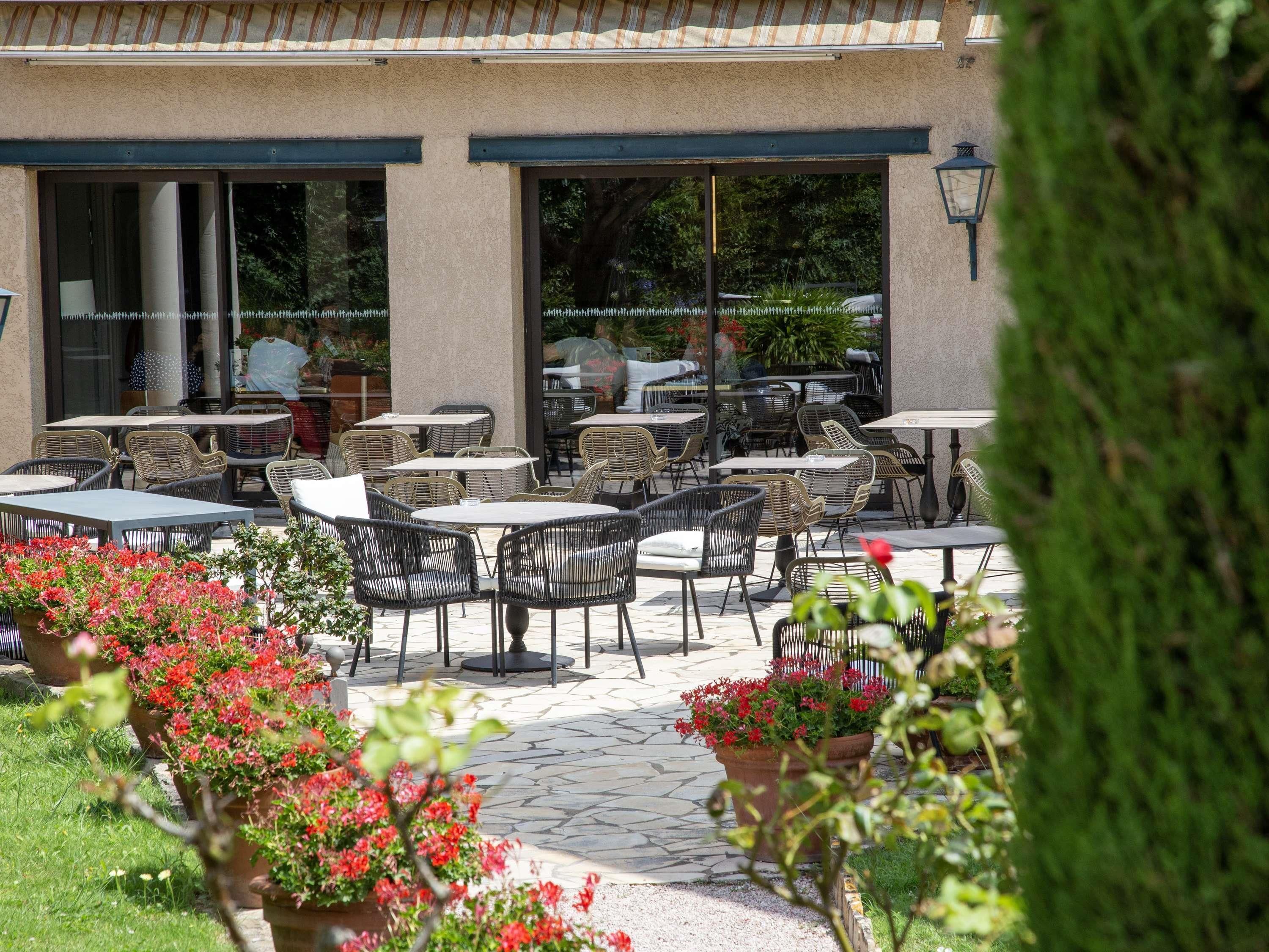 An outdoor patio with tables and chairs, surrounded by potted plants and a stone-tiled floor.