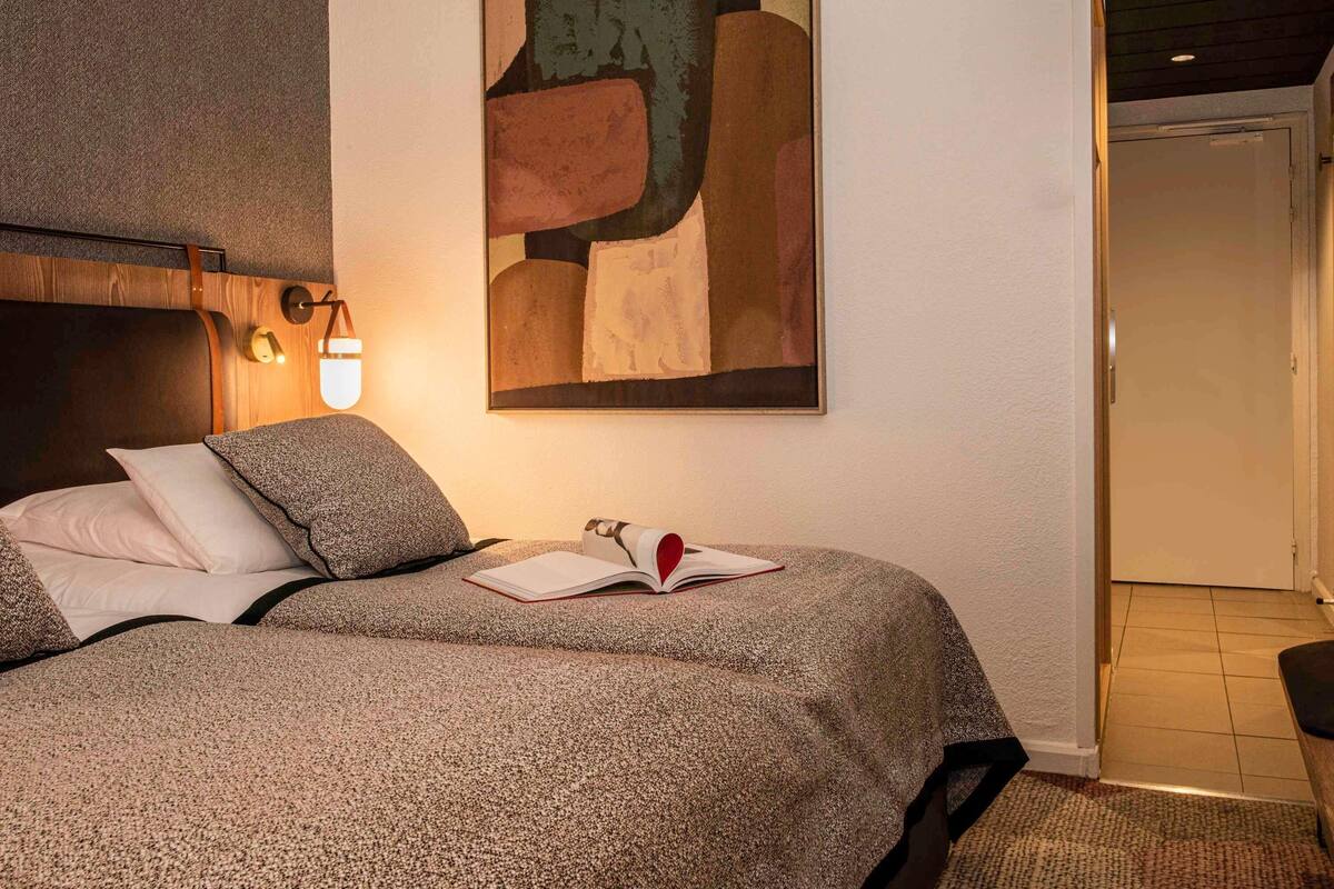 Ein Schlafzimmer mit einem Bett, einem Wandbild im abstrakten Stil, einem Nachttisch mit einem Buch und einem Beistelltisch.
