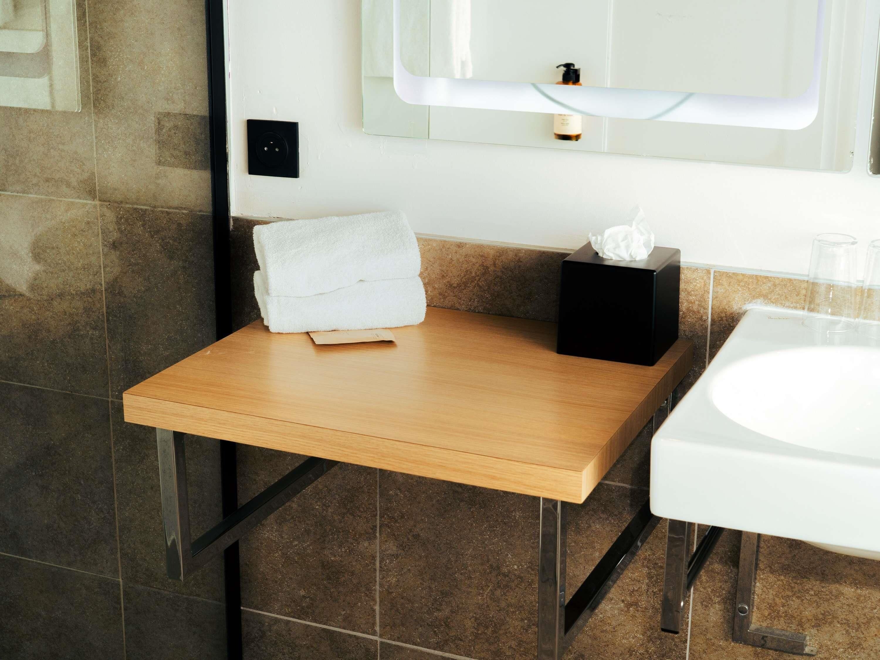 A bathroom with a wooden vanity, a white sink, and a towel on the counter.