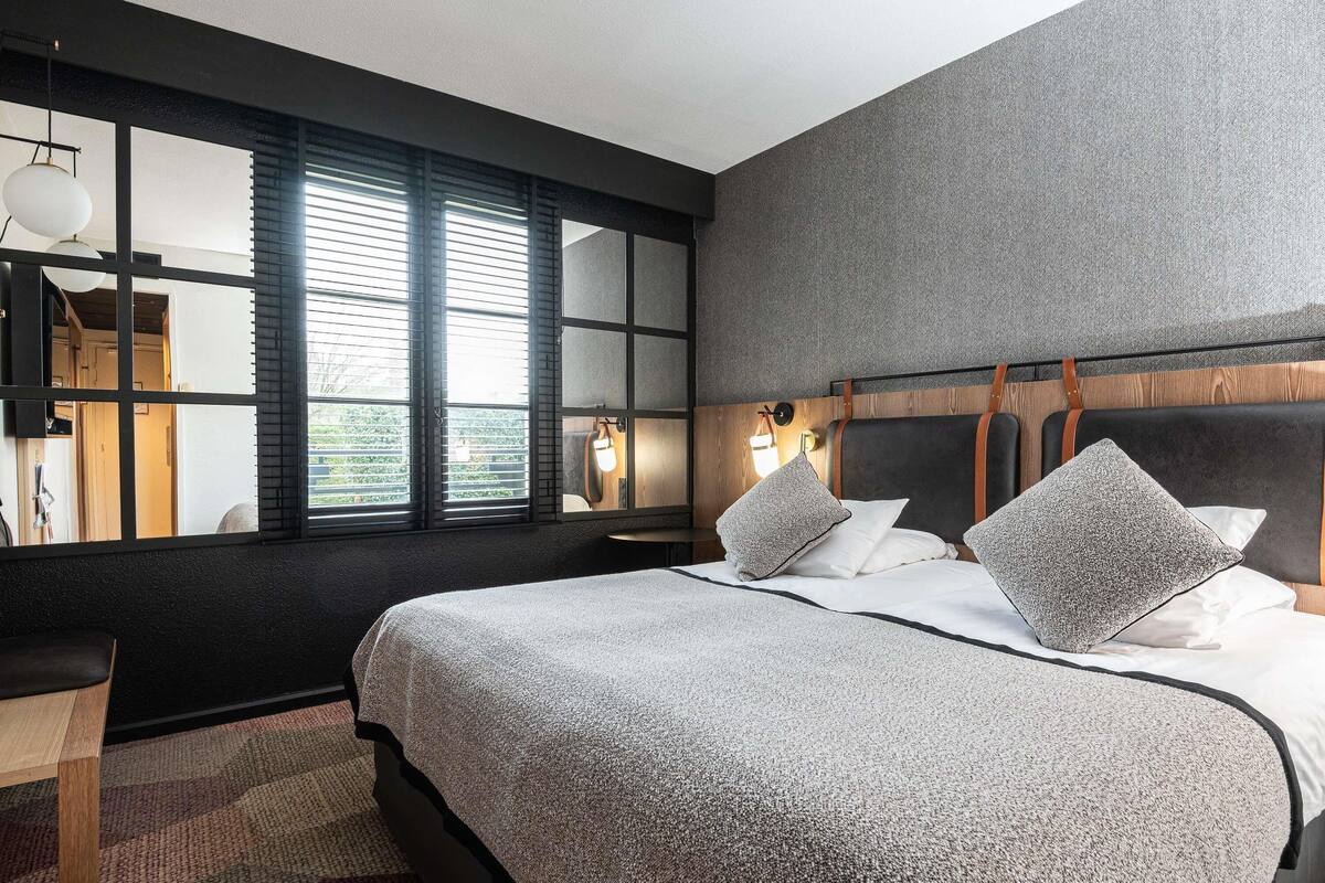 Ein modernes Hotelzimmer mit einem großen Bett, einem Schreibtisch und Blick durch raumhohe Fenster.