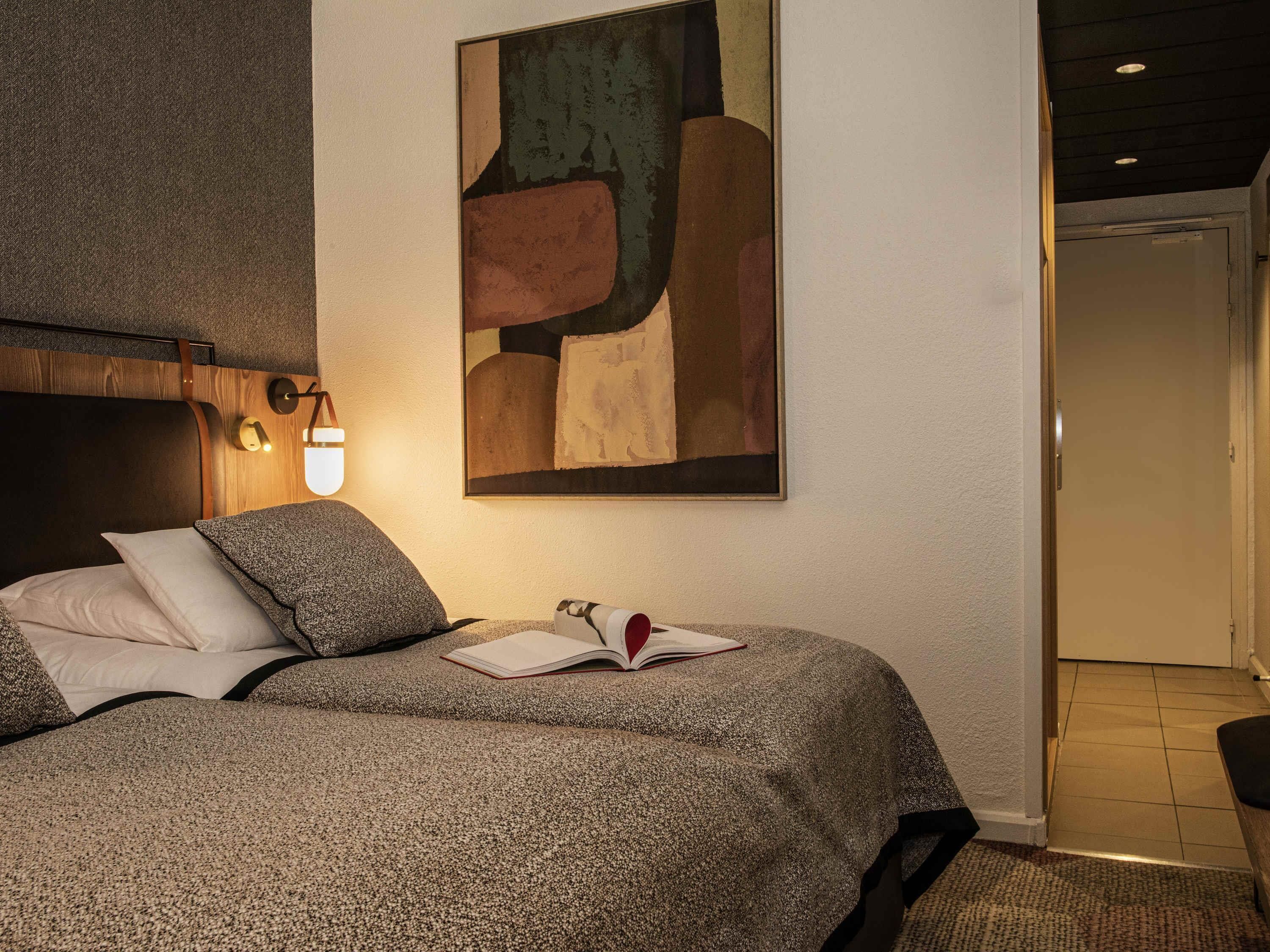 Un dormitorio con una cama, un cuadro abstracto colgado en la pared, una lámpara de noche y una puerta que da a otra habitación.
