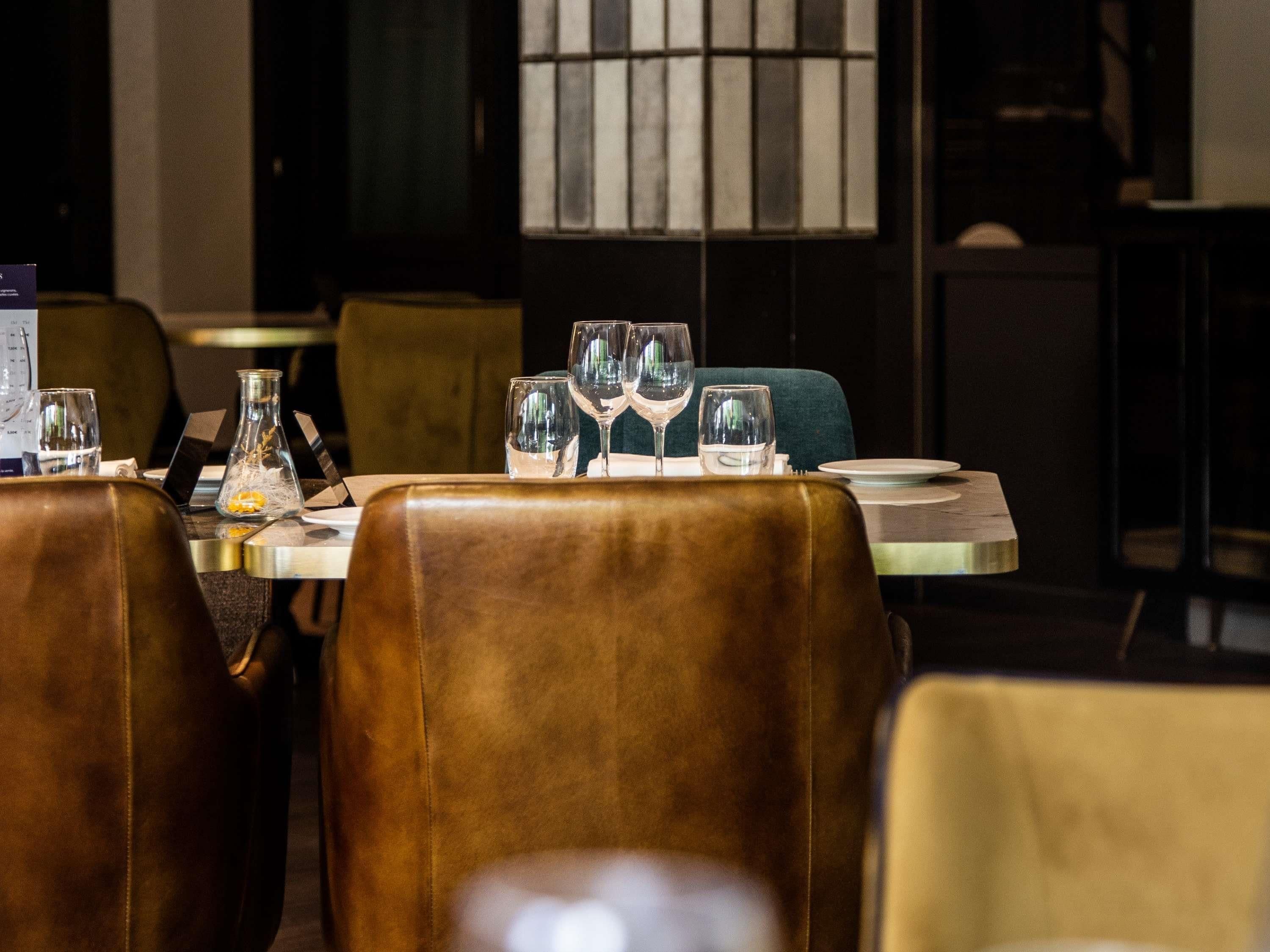 Un coin repas avec des fauteuils en cuir, une table dressée avec des verres à vin, un vase contenant des fleurs séchées et un menu posé sur la table.