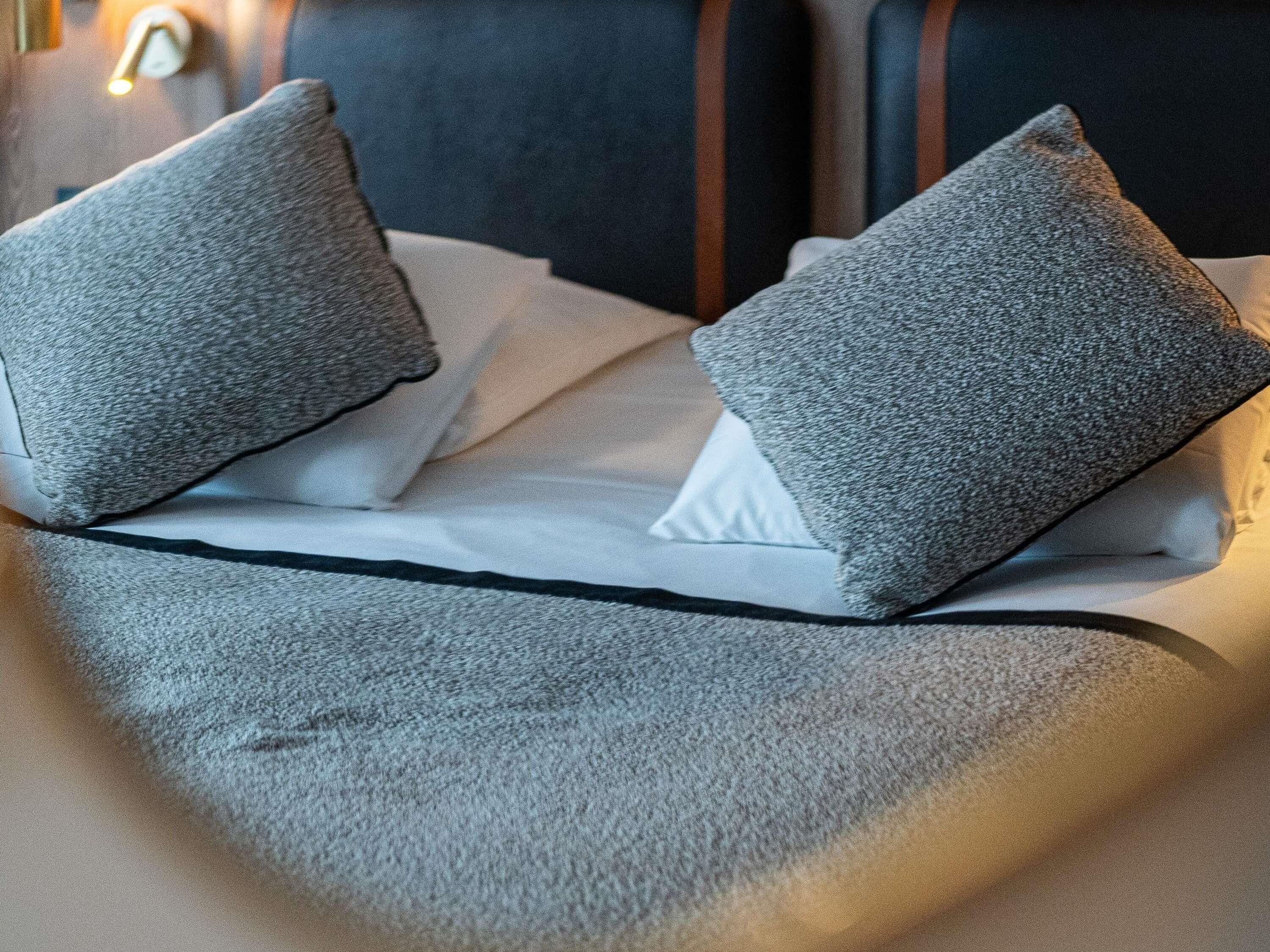 Una cama con almohadas grises y sábana blanca.
