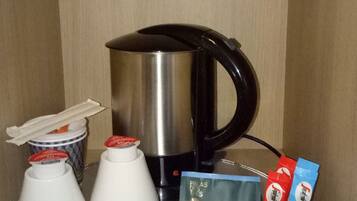Un equipo de minibar con cafetera, dos tazas y varios sobres de bebidas.