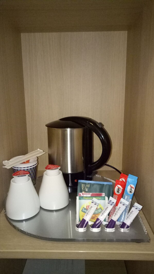 Un mini-bar équipé d’une machine à café, de deux tasses et de plusieurs sachets de boissons.