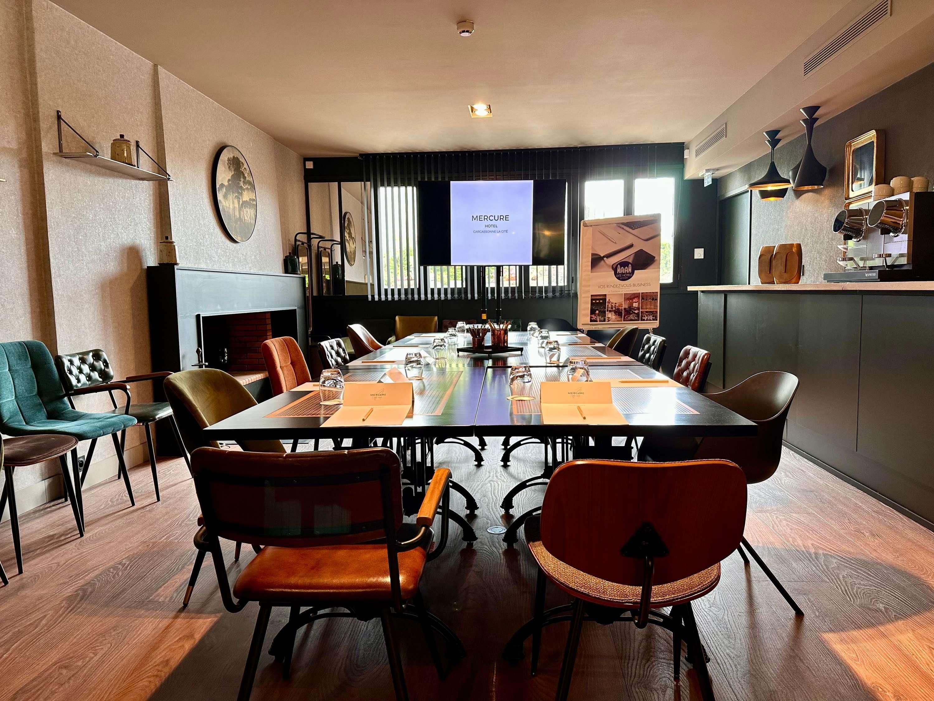 Un salón de conferencias con una larga mesa, sillas, una chimenea y una pantalla de proyección.
