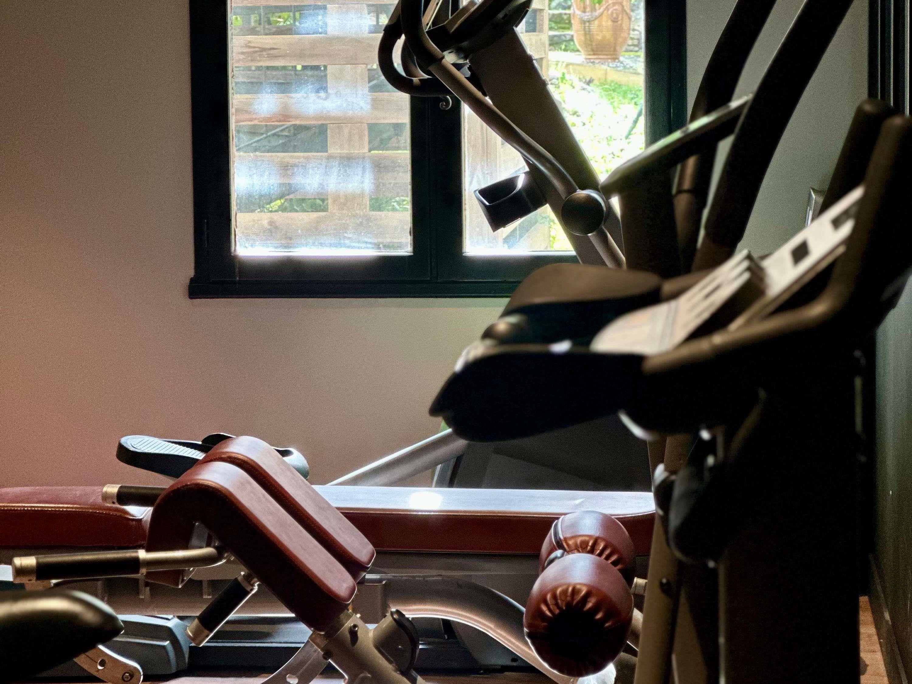 Une salle de sport équipée de matériel d’exercice, une fenêtre donnant sur des immeubles et une porte.