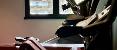 Une salle de sport équipée de matériel d’exercice, une fenêtre donnant sur des immeubles et une porte.