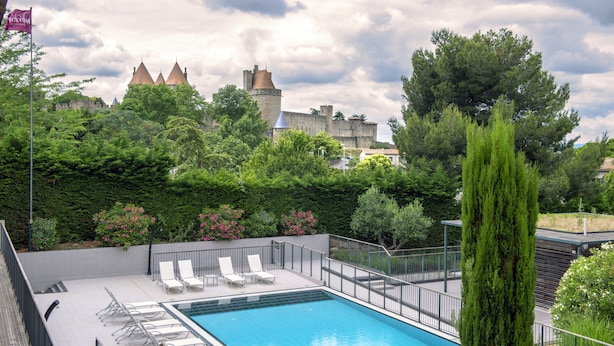 Una piscina con sillones de descanso, rodeada de follaje y un castillo al fondo.