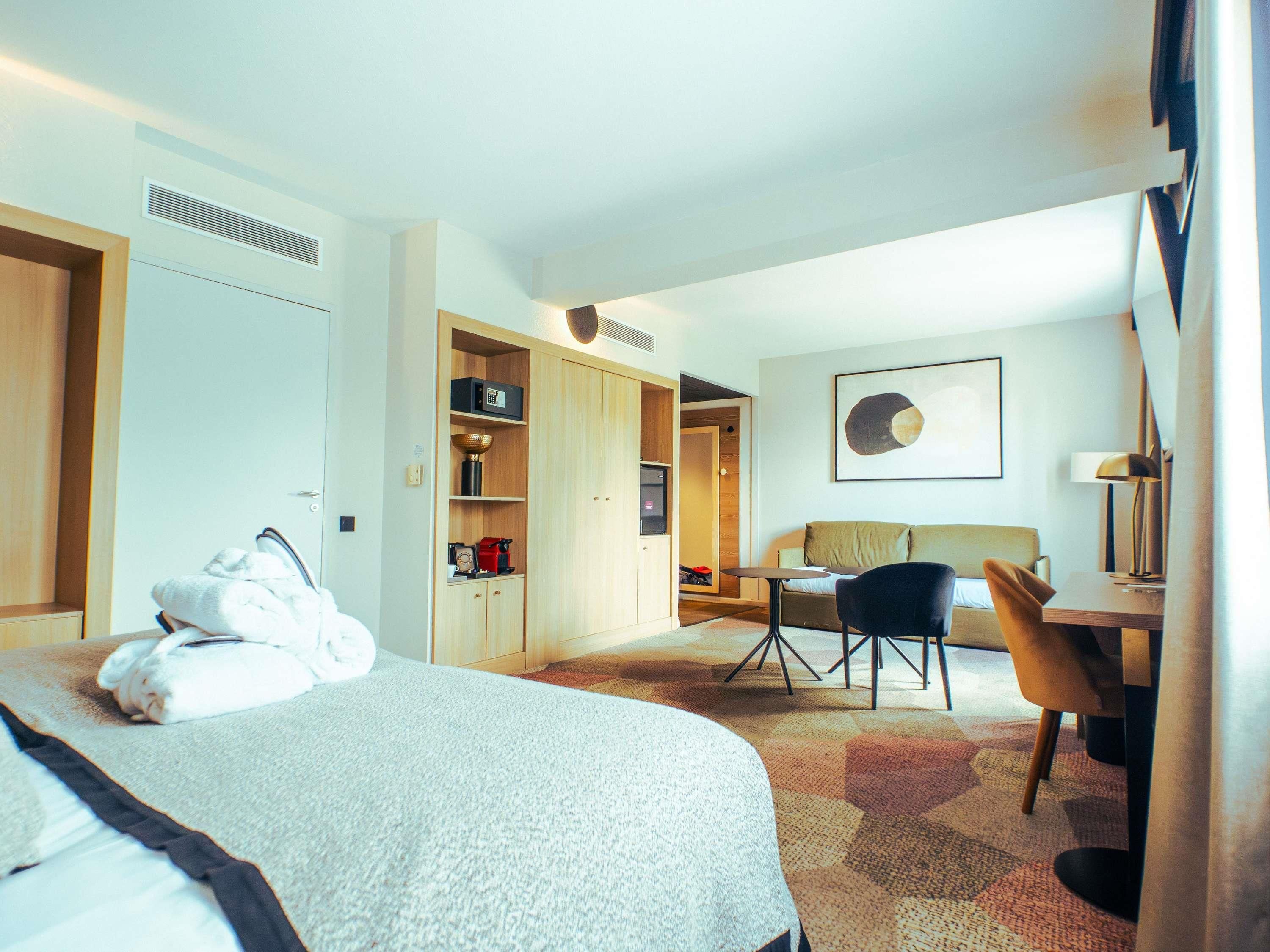 A hotel room with a bed, a desk, a chair, a sofa, a coffee machine, and a microwave.