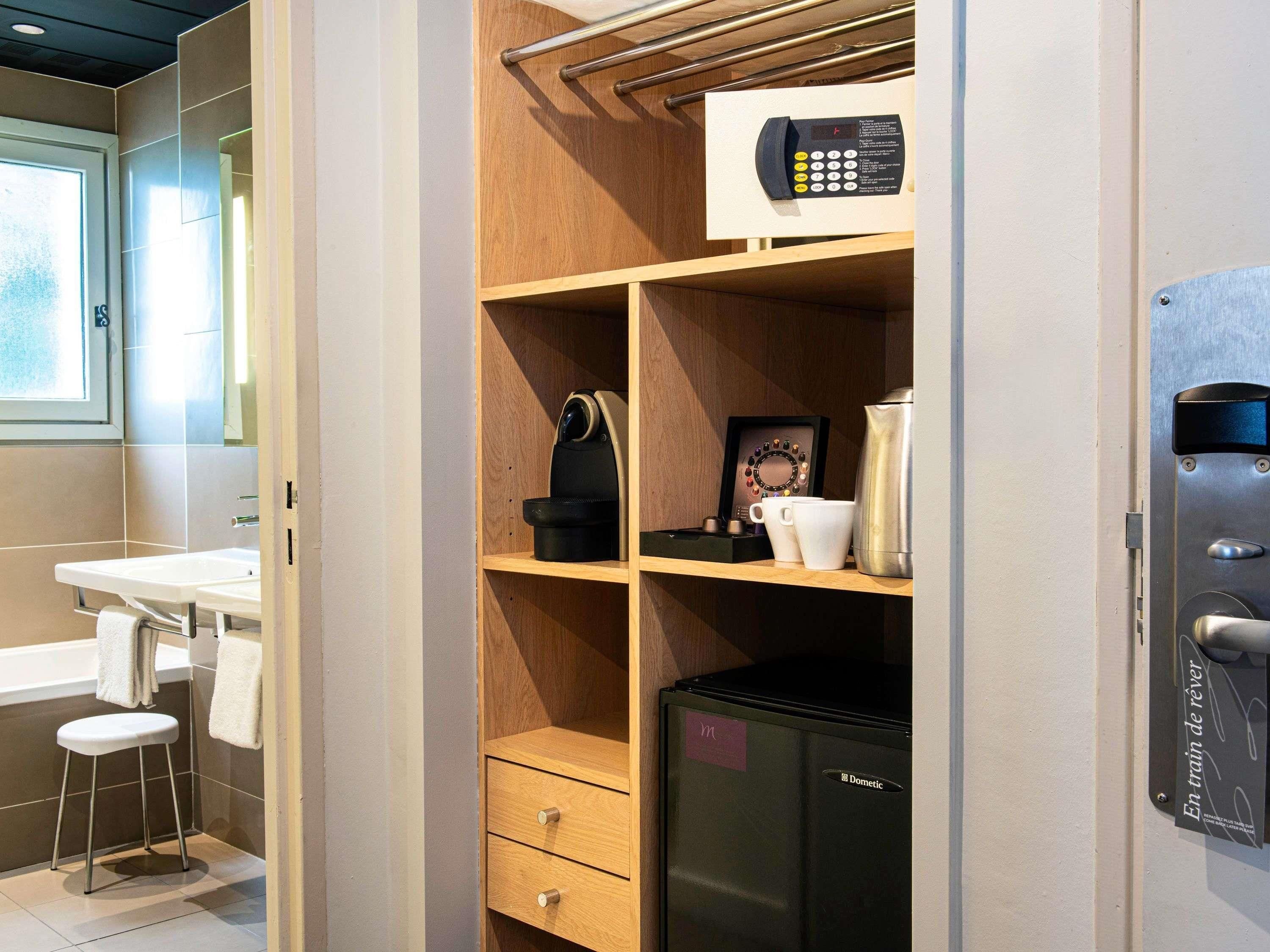 A compact bathroom with a sink, a stool, a towel rack, a microwave, a kettle, and a small refrigerator.