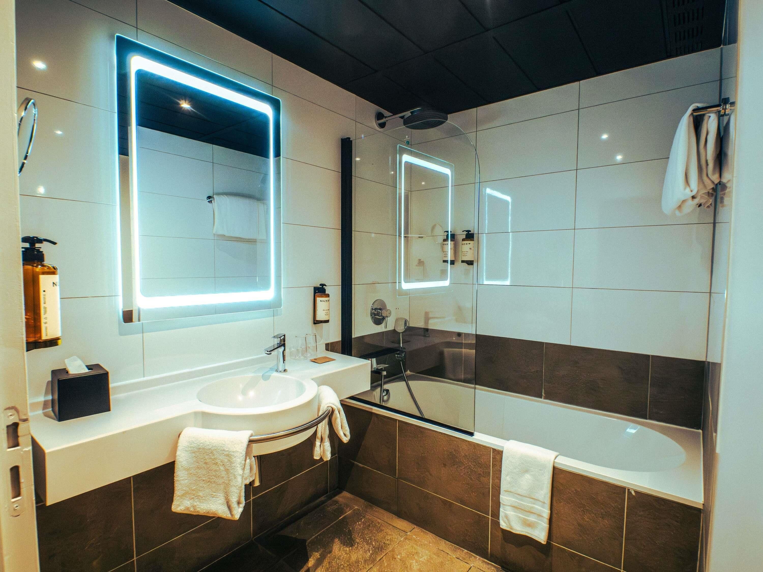 Ein modernes Badezimmer mit einem weißen Waschbecken, einem großen Spiegel und einer Badewanne.