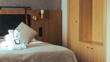 A hotel room with a bed, a wooden wardrobe, a wall clock, and a bedside table.