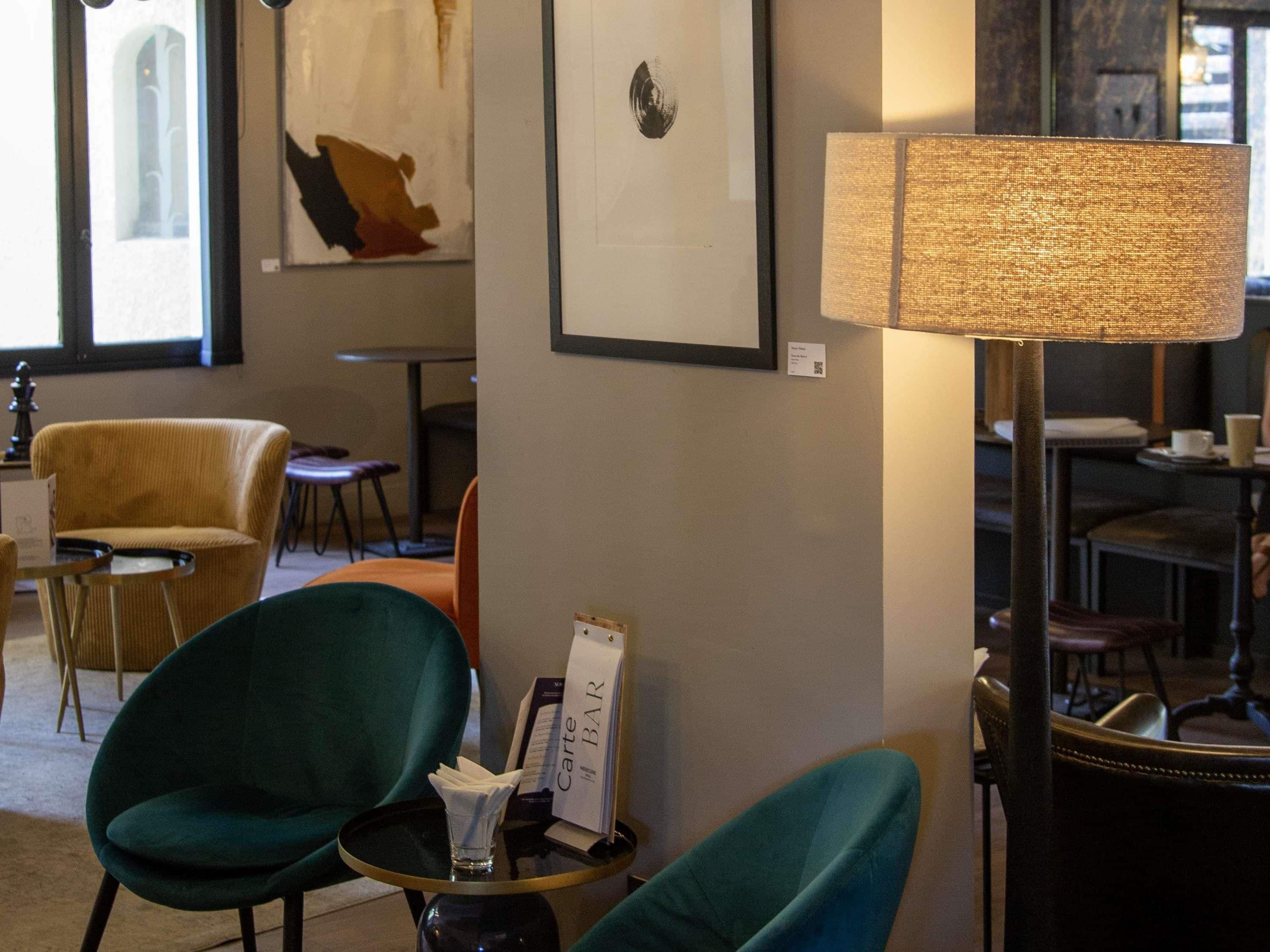 A cozy seating area with two green chairs, a small table with a lamp, and a framed artwork on the wall.