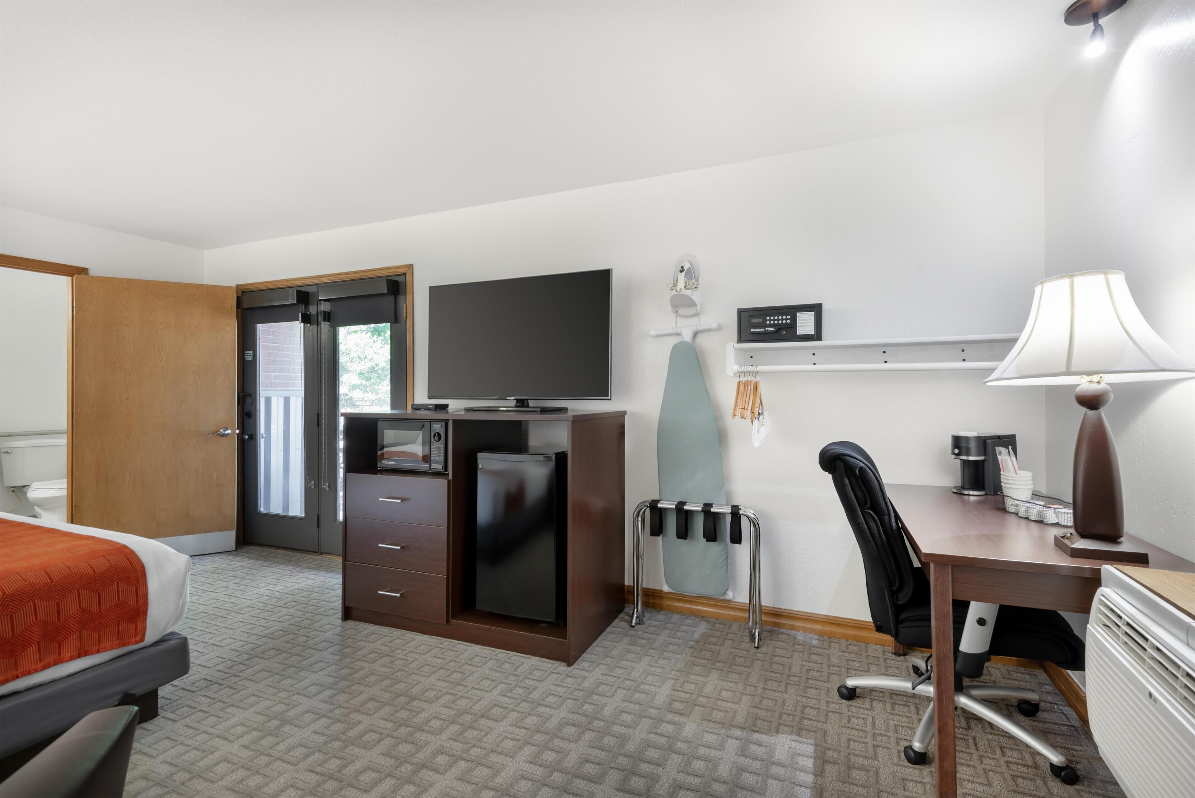 A hotel room with a bed, a desk, a television, a mini-fridge, a coffee maker, and a lamp.
