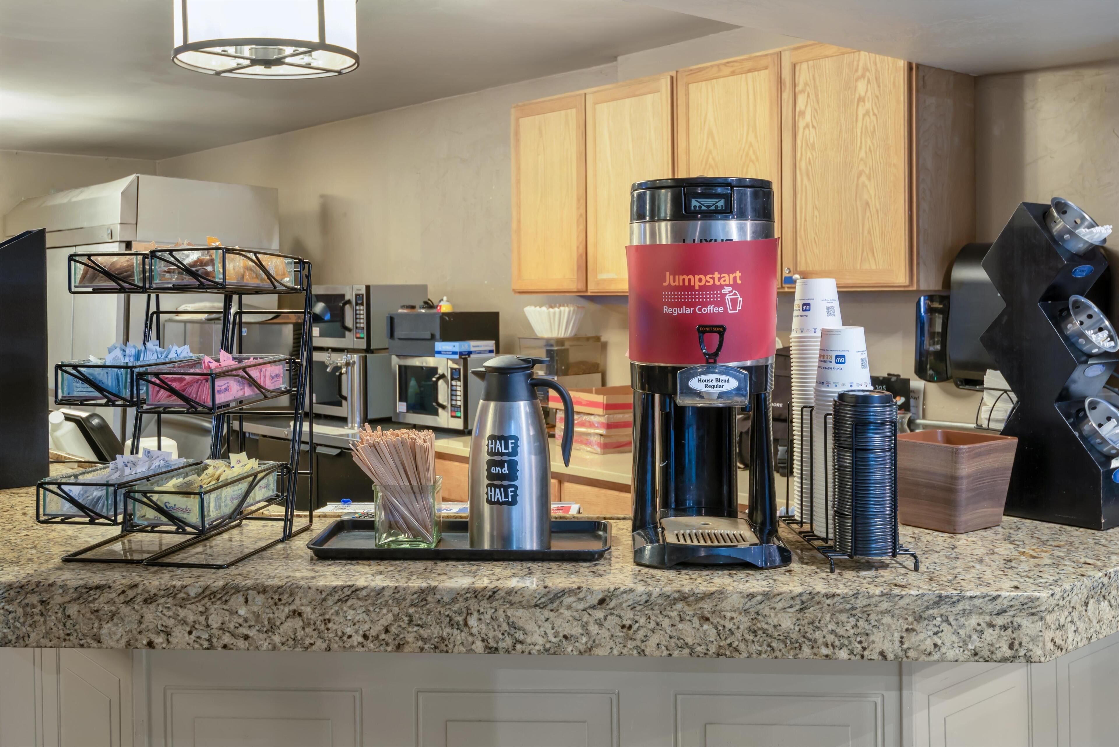 A kitchen area with a coffee station, including a coffee maker, a kettle, and a coffee dispenser.