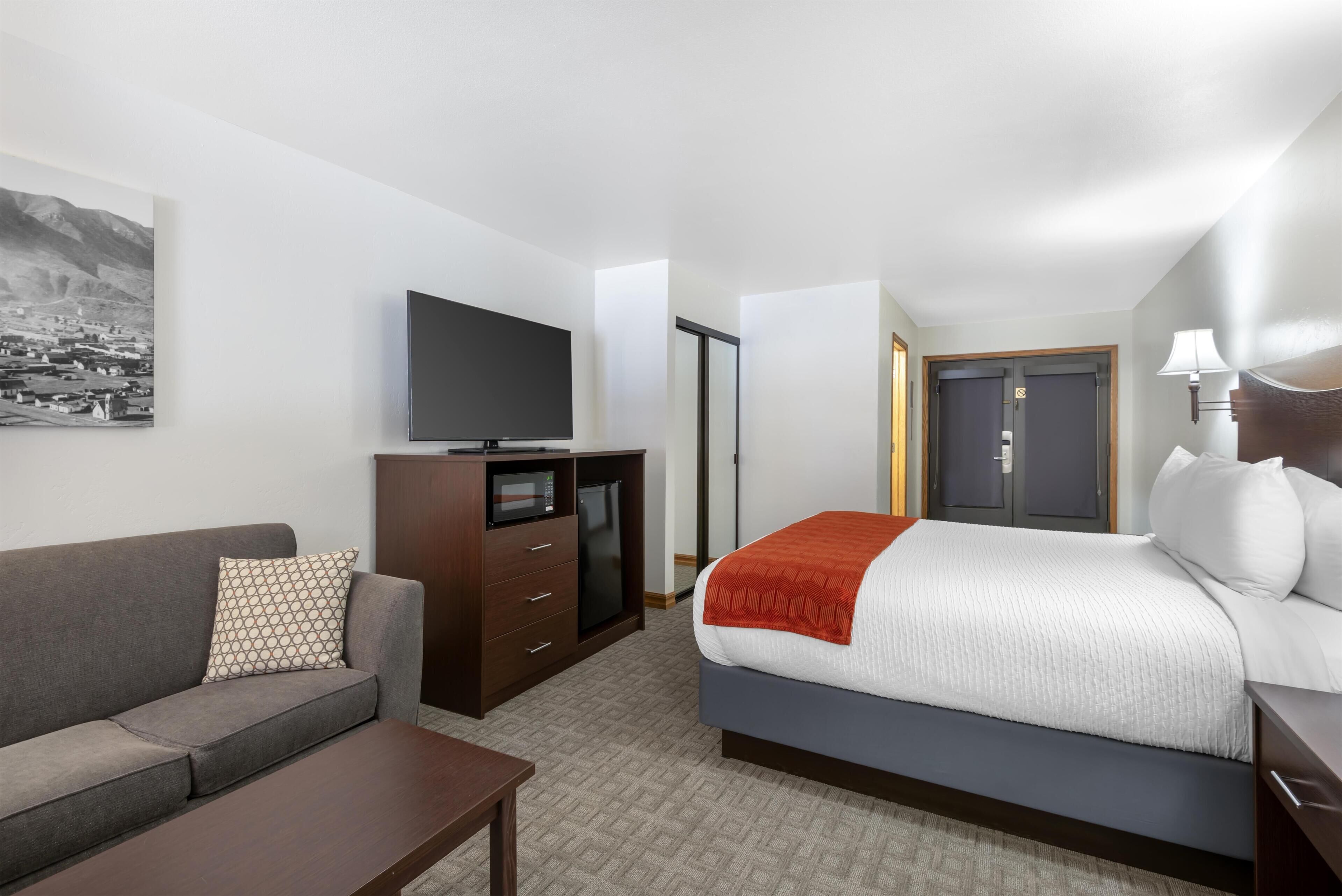 A hotel room with a bed, a sofa, a TV, a desk, and a wardrobe.