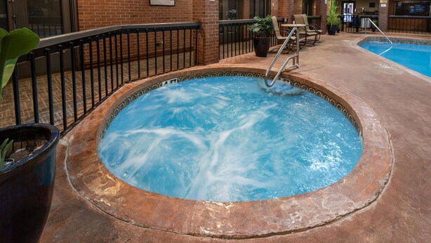 A hot tub with a metal railing, surrounded by a brick wall and potted plants.