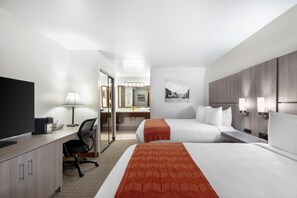 A hotel room with a desk, two beds, a TV, a lamp, a mirror, and a picture on the wall.