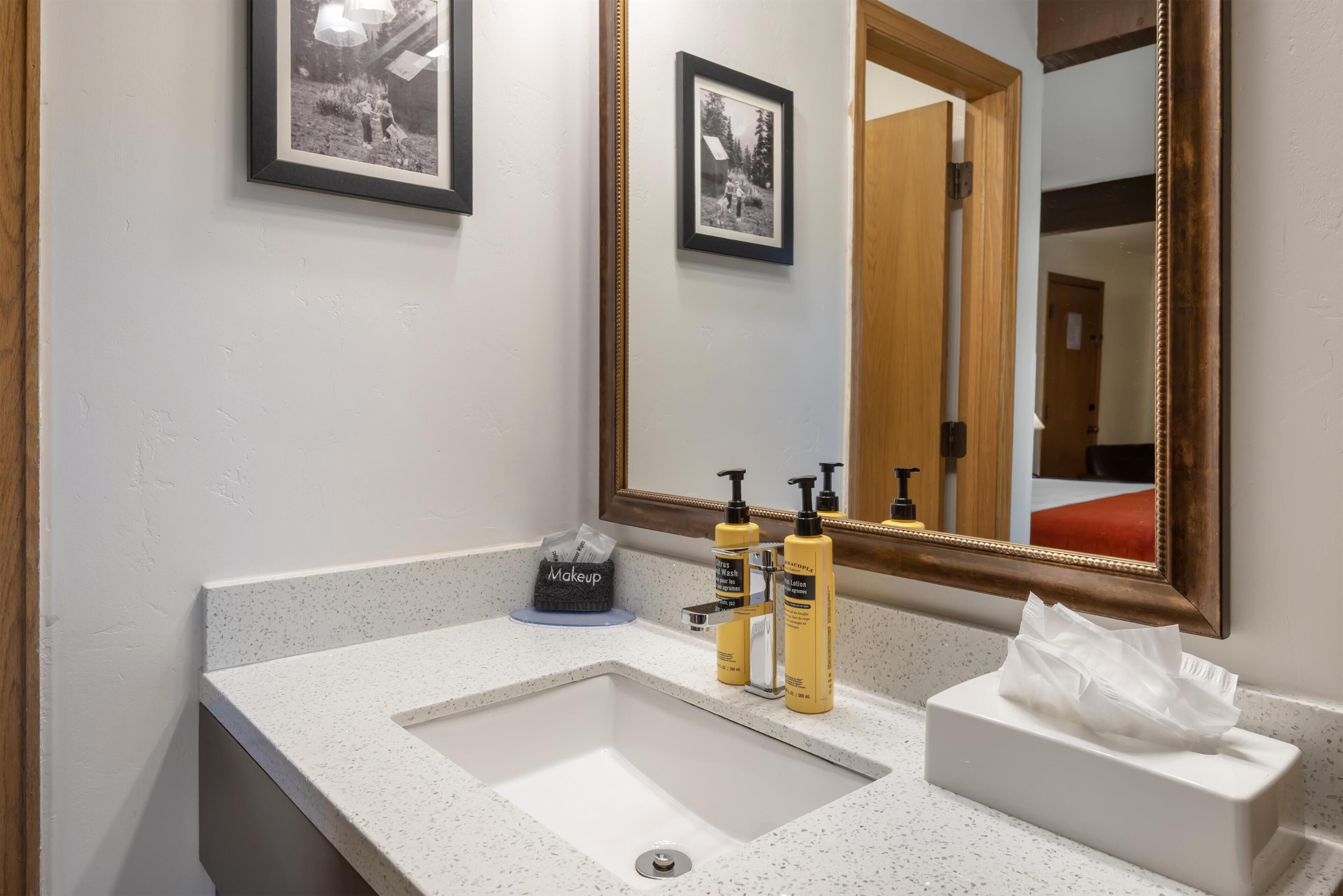 A bathroom with a white sink, a mirror, and framed pictures on the wall.