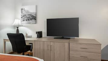 A hotel room with a bed, a desk with a chair, a television, a lamp, and a picture on the wall.