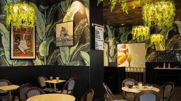 Interior de restaurante con techos altos, plantas colgantes y una pizarra de menú. Mesas y sillas dispuestas para comer.