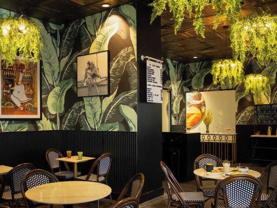 Interior de restaurante con techos altos, plantas colgantes y una pizarra de menú. Mesas y sillas dispuestas para comer.