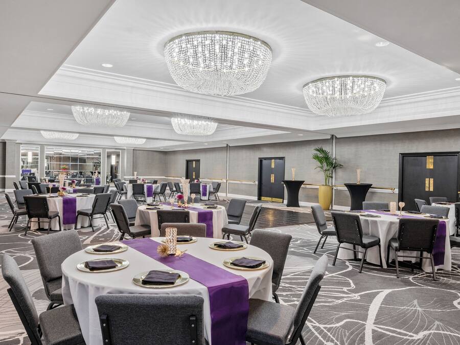 A banquet hall with round tables, purple tablecloths, and chandeliers.