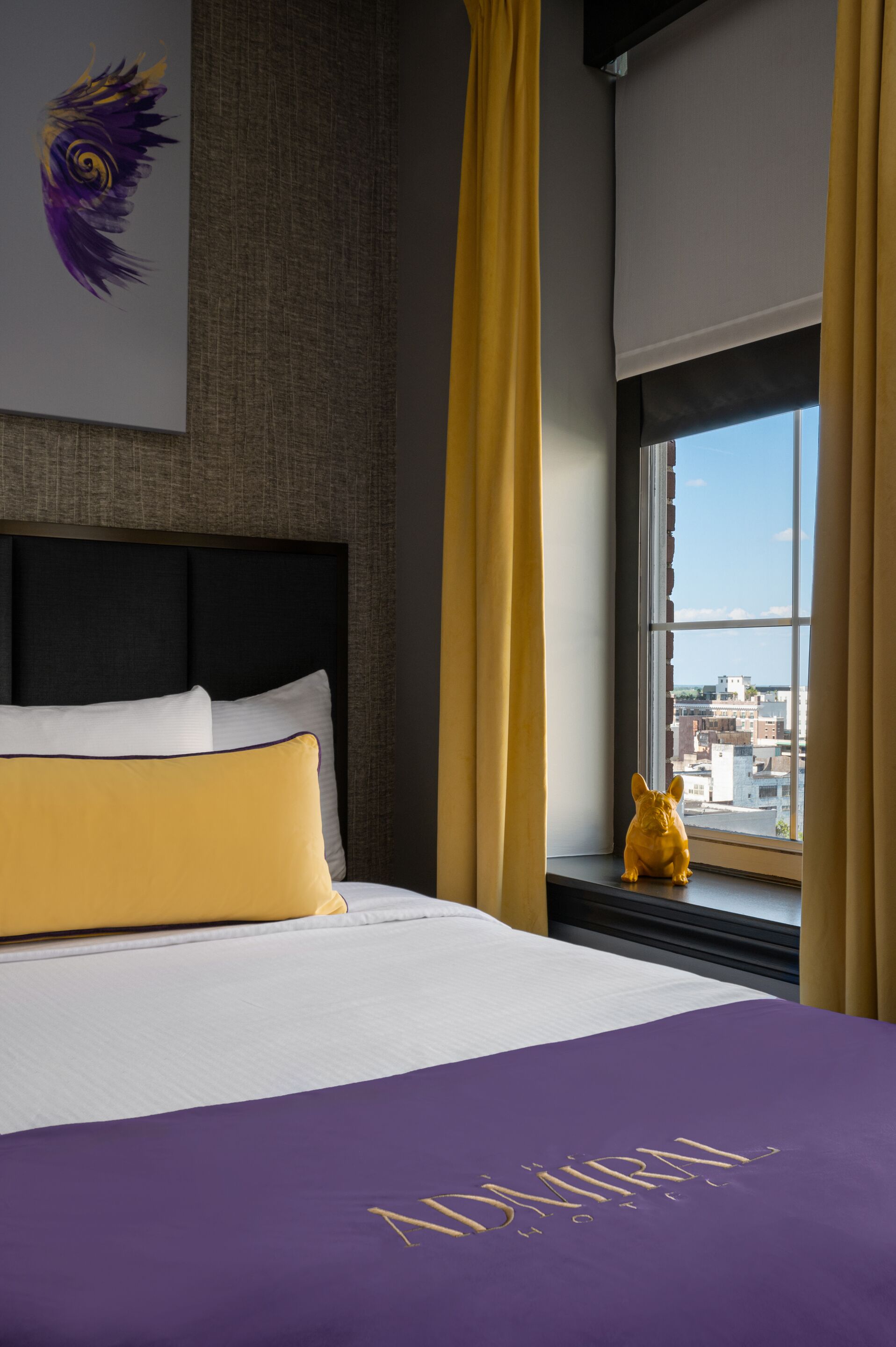 A hotel room with a bed, a view of the city through a window, and a decorative item on the windowsill.