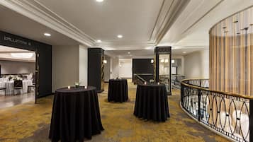 A hotel lobby with round tables covered in black cloth, a staircase, and a decorative railing.