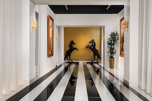 Un pasillo pulido con piso a cuadros blanco y negro, dos esculturas de bronce de caballos y una gran pared dorada.