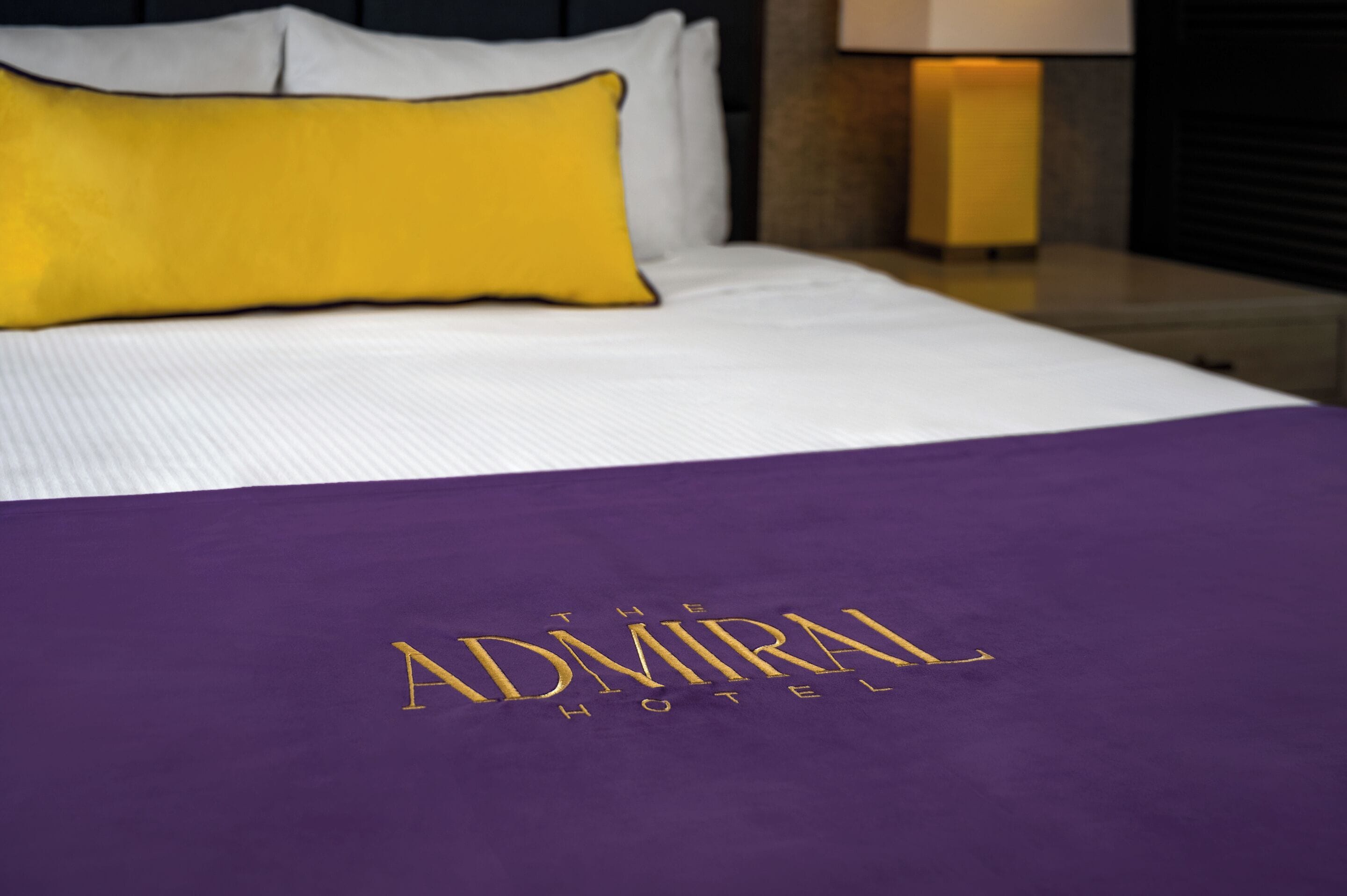 Een bed met een paars dekbed en een geel kussen.