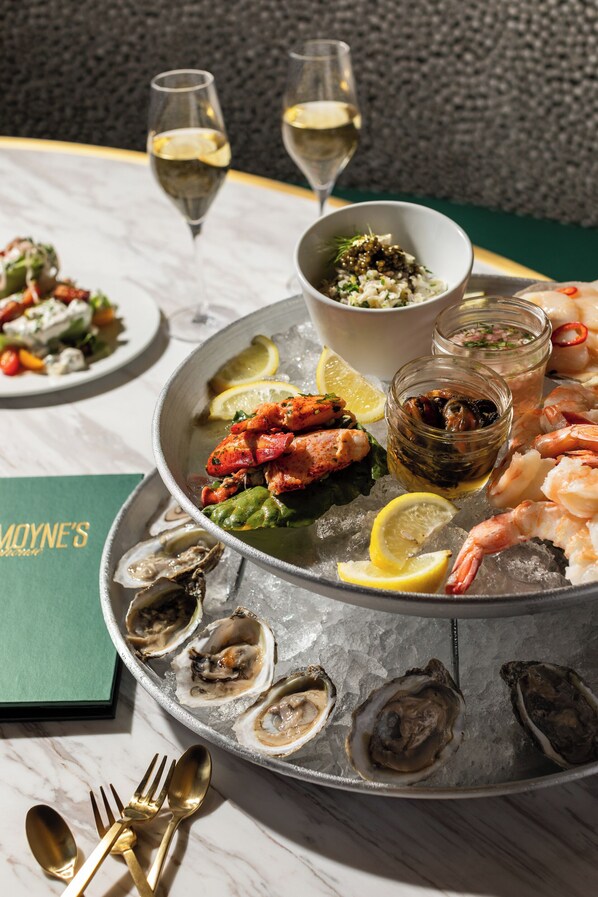 A seafood platter with oysters, shrimp, and lobster on ice, accompanied by glasses of white wine and a bowl of salad.