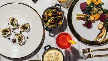 A dining table with plates of food, a pot of vegetables, and a glass of drink.