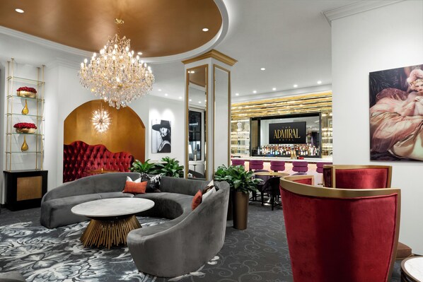 A modern hotel lobby with a grand chandelier, a bar area, and plush seating.